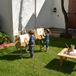 Two children painting on easels in a yard.